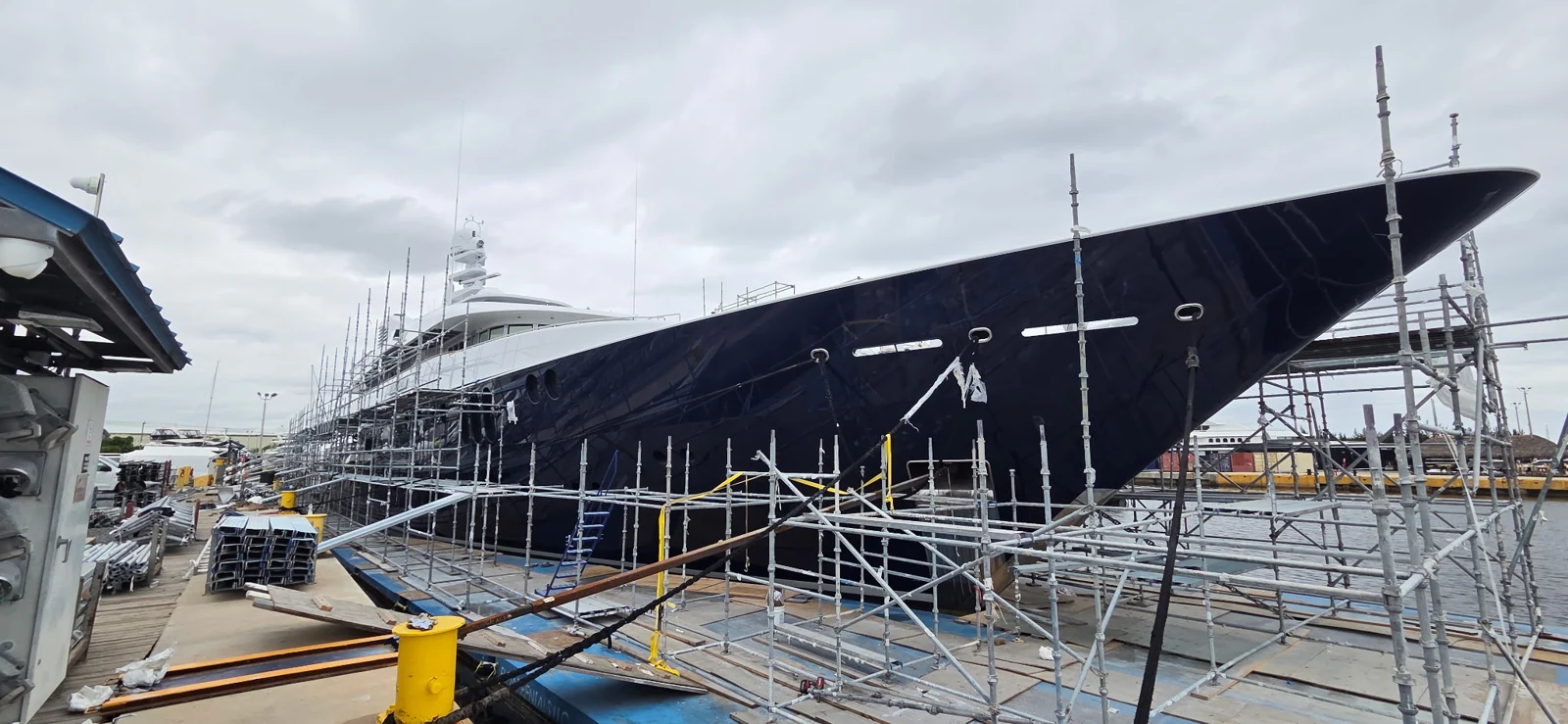 Scaffolding surrounding a dark-blue yacht hull for painting and refinishing